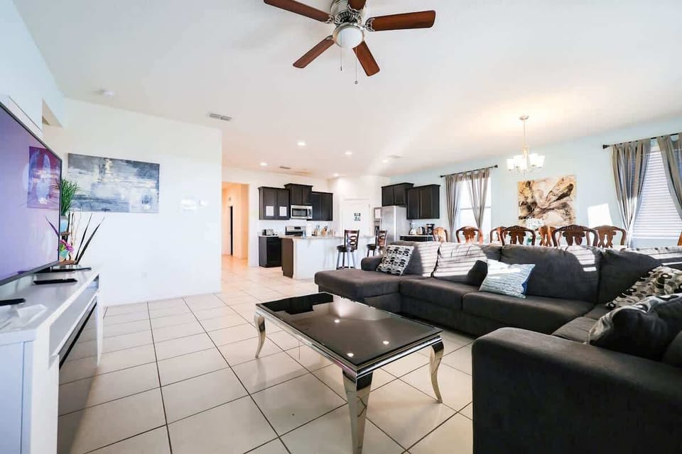 Spacious and bright first-floor living room with an open layout, featuring a sofa and TV area, dining space, kitchen, and glass doors overlooking the pool.