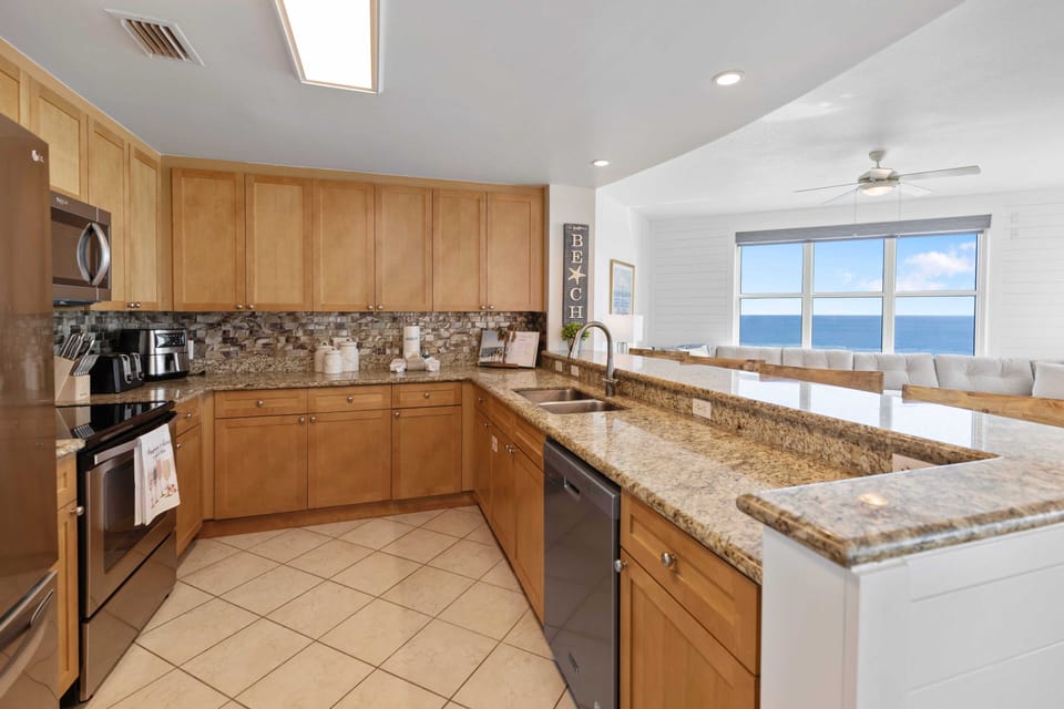 Cook with ocean views streaming through expansive windows in your fully equipped kitchen with granite counters and modern appliances.
