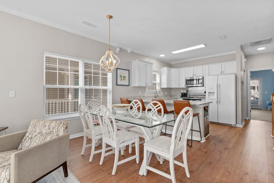 Your elegant open-concept space combines dining and kitchen with rich hardwood floors, bright white cabinetry, and stylish pendant lighting creating the perfect gathering spot.