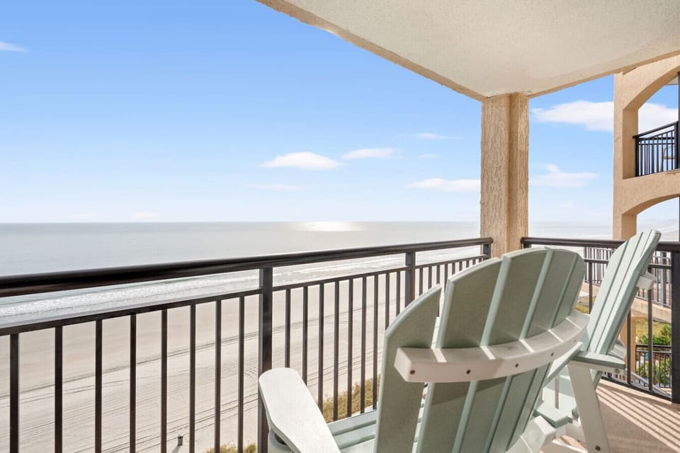 Private oceanfront balcony with raised Adirondack chairs overlooking the resort pools and the North Myrtle Beach coastline. The perfect spot to relax, sip coffee, and enjoy sweeping ocean views.