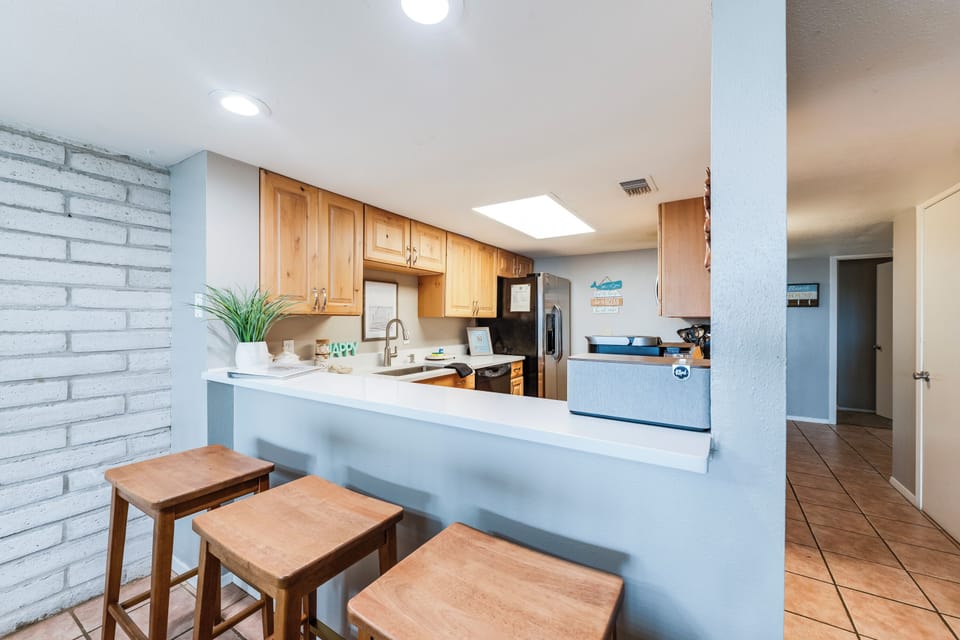 Combined living and dining area with leather sofas, wooden dining table, TV cabinet, brick accent wall, and large shuttered windows. Designed for your group or family to gather, eat, and relax together.