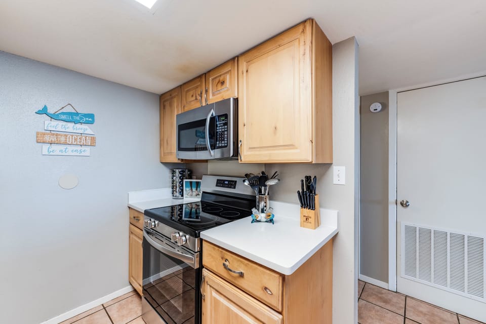Kitchen area with light wood cabinets, white countertops, full-size appliances, and a coffee maker, opening to a dining table with seating for a group. Designed to make cooking for up to 10 guests easy.