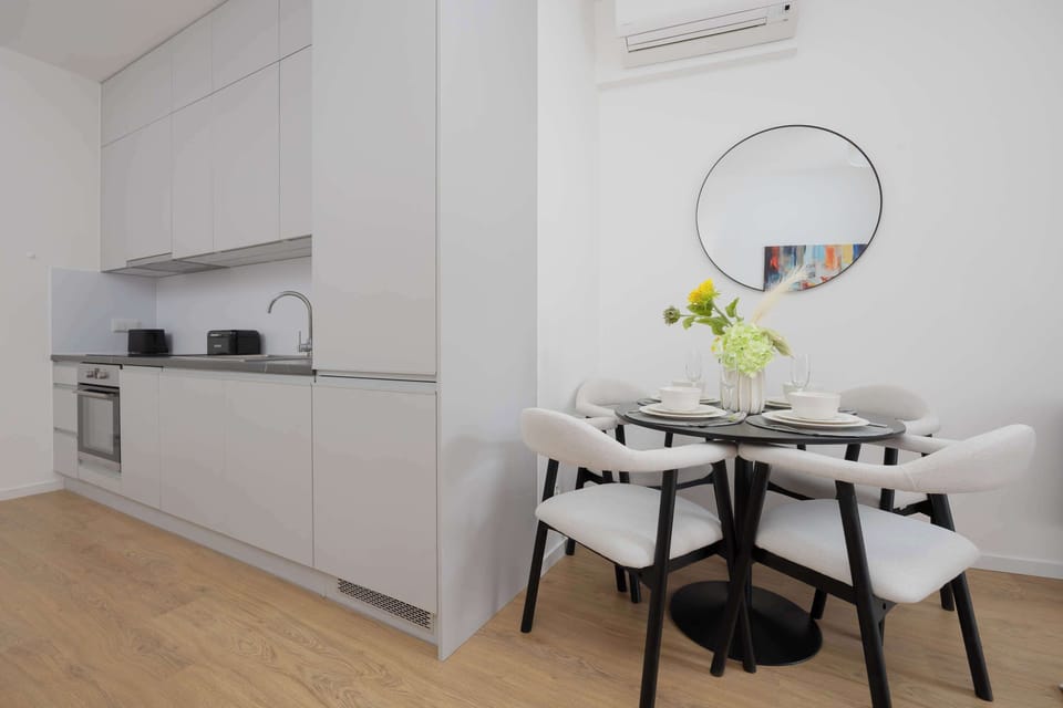 An open-plan view combining the kitchen and dining area. White cabinets and minimal decor create a modern look. The space feels bright and functional.
