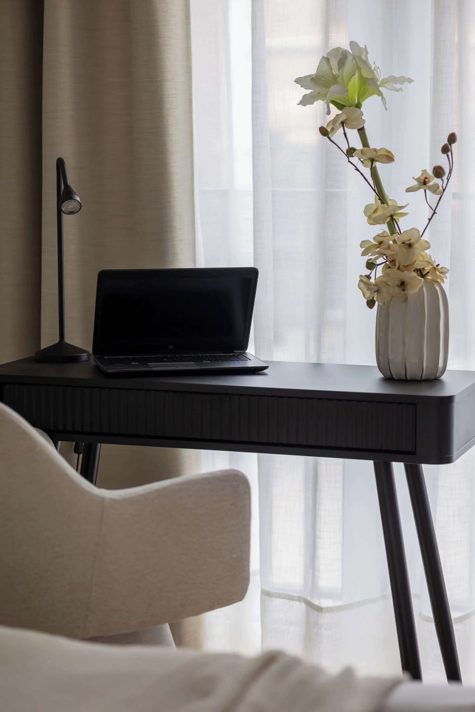 A workspace or vanity area with a black desk and chair near the bed. Decorative elements add warmth. The setup feels functional and elegant.