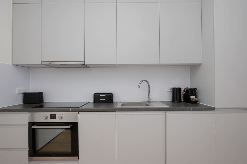A white kitchen with built-in appliances and sleek cabinetry. The countertops are uncluttered. The design emphasizes simplicity and cleanliness.