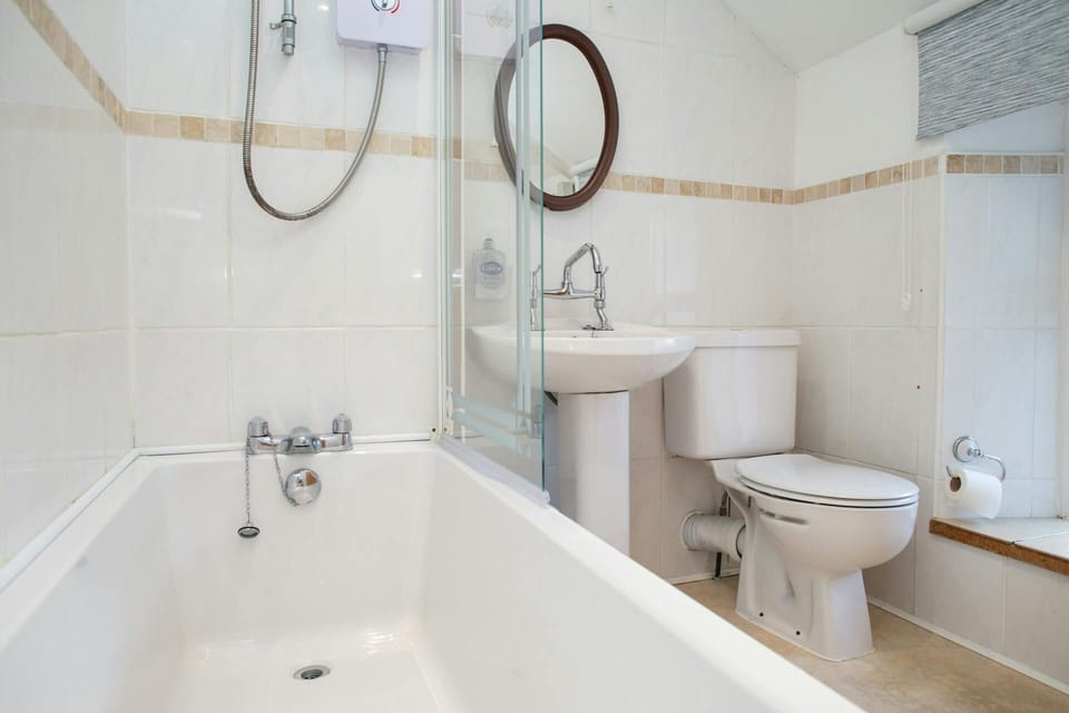 Toilet and sink next to bathtub with wall-mounted shower unit