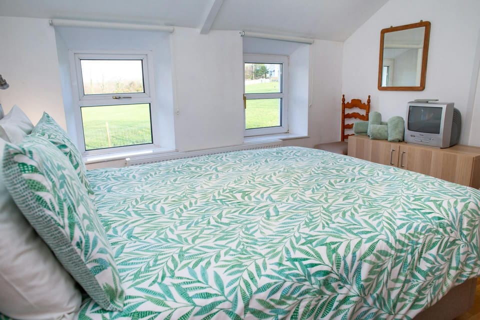Bedroom with double bed, leaf-pattern duvet and pillows, and two windows