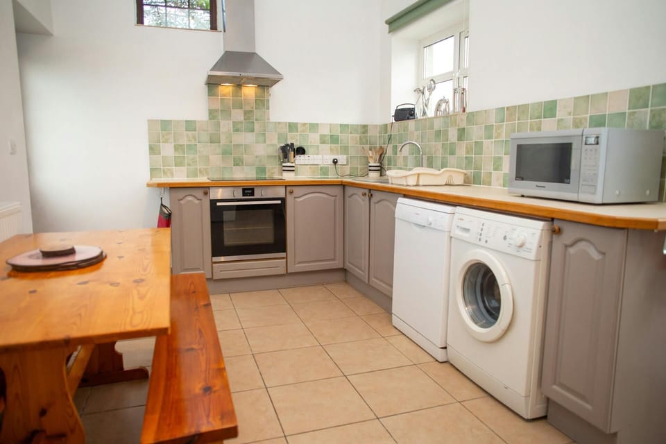 Open-plan kitchen with cooker hood, tiled splashback and wooden dining bench