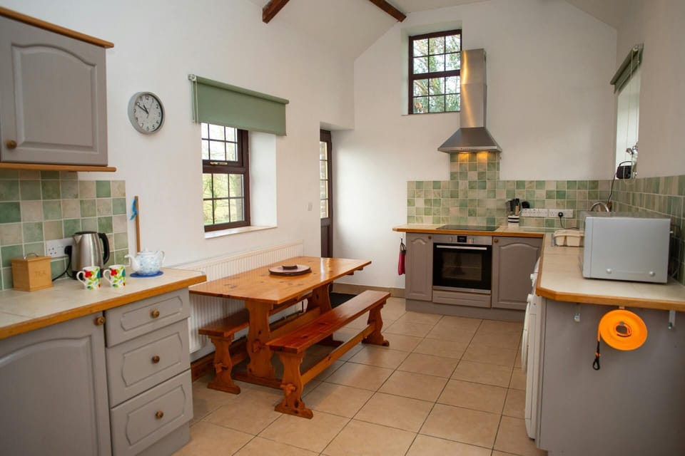 Kitchen with wooden dining table and benches, tiled floor and green tile splashback