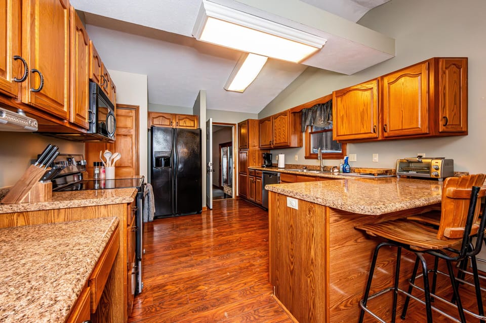 Granite countertops stretch along oak cabinetry in the kitchen, paired with black appliances and wood flooring.