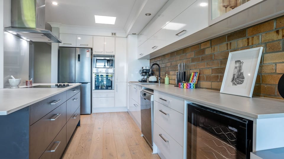 Fully equipped modern kitchen with stone benchtops, dishwasher, and brick splashback