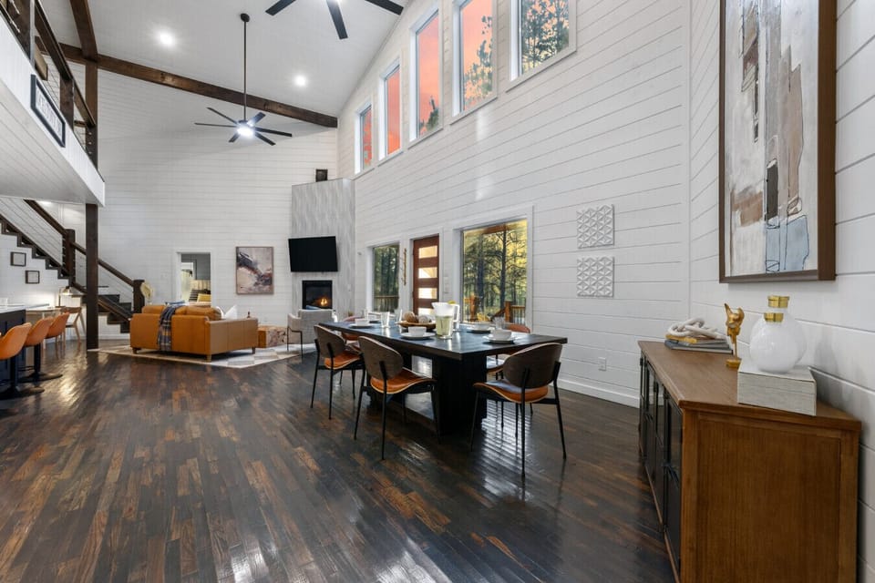 Vaulted great room with exposed ceiling beams, ceiling fan, loft above, and cozy orange sectional — plenty of room for 14 guests to relax and unwind.