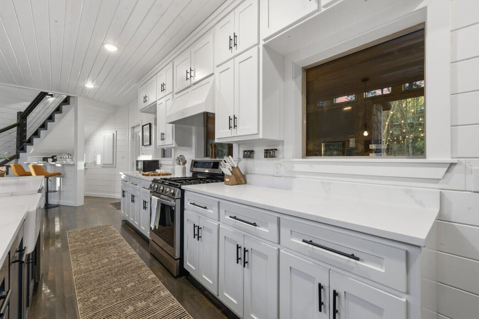 Chef`s kitchen with quartz waterfall island, custom navy cabinetry, professional gas range & designer pendant lighting — fully stocked for groups and family gatherings.
