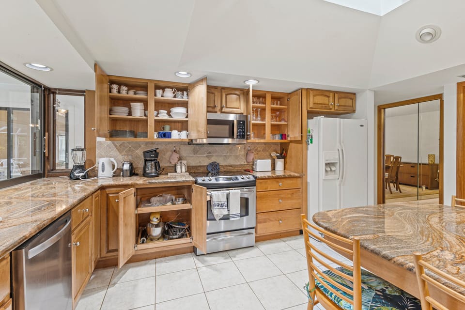 The kitchen has granite countertops and an open floor plan with the living room and includes a fridge, stove, oven, microwave, dishwasher, blender, coffee maker, cooking utensils, dishware and seating for eight.