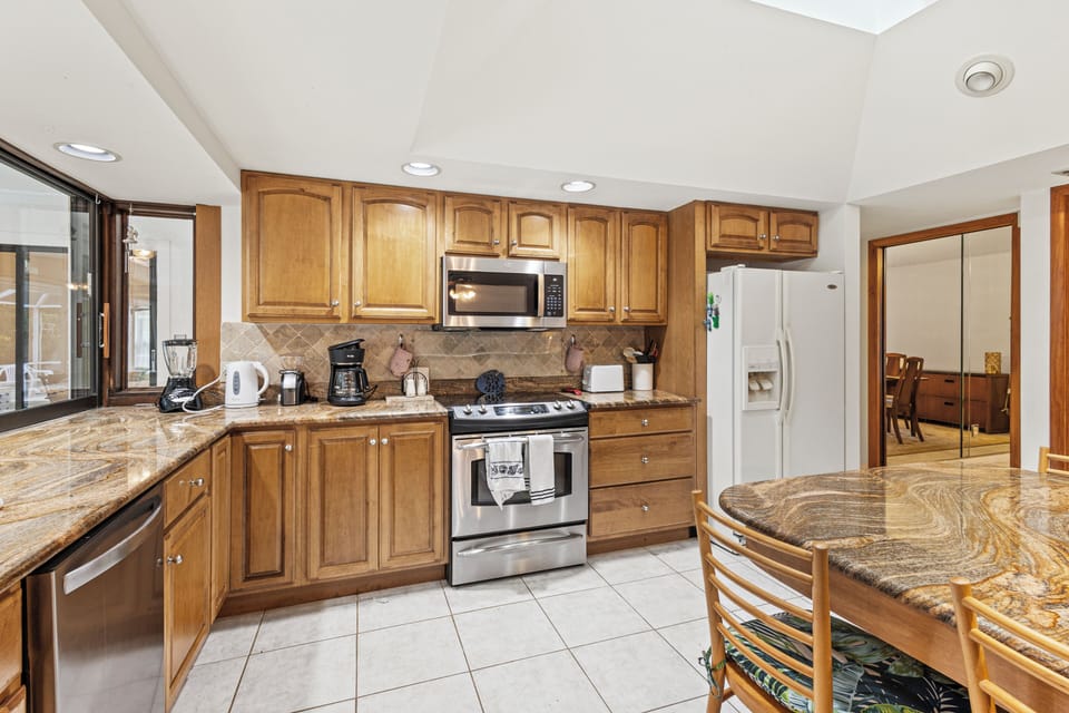 The kitchen has granite countertops and an open floor plan with the living room and includes a fridge, stove, oven, microwave, dishwasher, blender, coffee maker, cooking utensils, dishware and seating for eight.