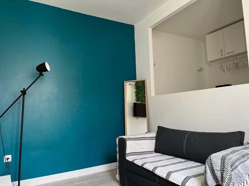 Coin salon avec canapé rayé, lampadaire noir et mur bleu canard — séjour lumineux du Coquet Toulouse