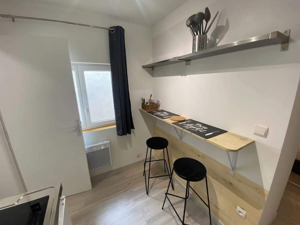 Vue sur la cuisine équipée — plan de travail, tabourets hauts et fenêtre avec lumière naturelle au Coquet
