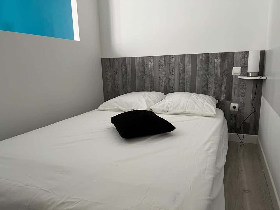 Lit double avec tête de lit en bois vieilli et linge blanc — espace nuit du studio Le Coquet Arènes