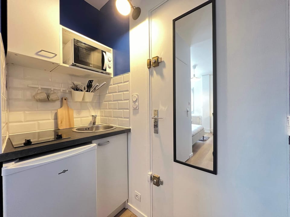 Détail de la kitchenette — plaques de cuisson, micro-ondes, réfrigérateur et crédence en carrelage métro blanc