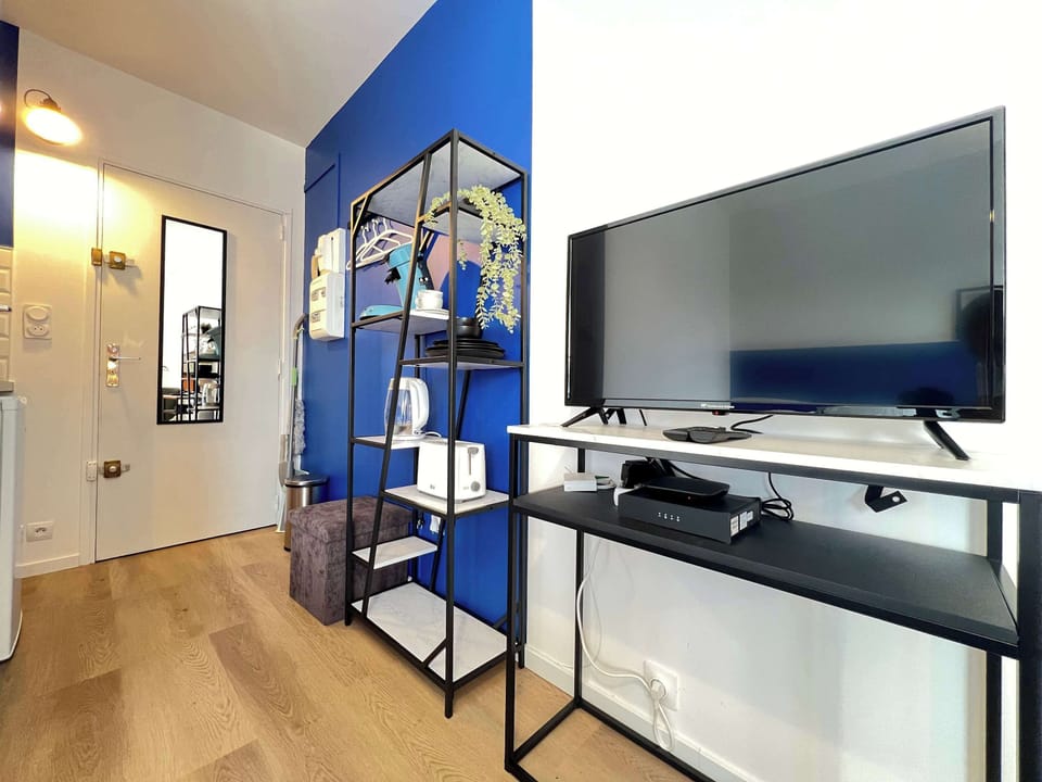 Télévision à écran plat et étagère décorative bleue — entrée du studio avec miroir et accès salle de bain