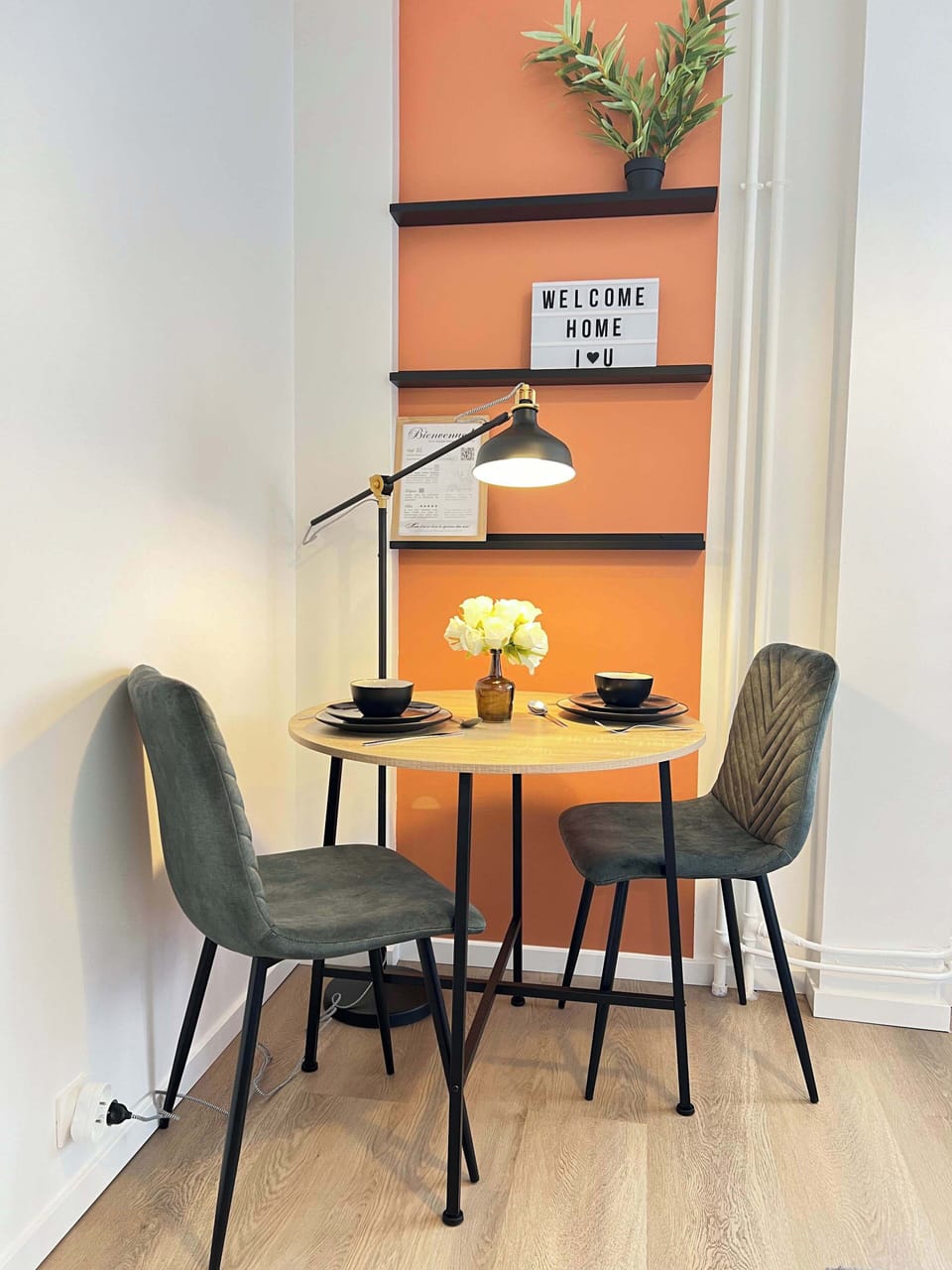 Espace repas pour deux personnes — table ronde, chaises et étagère décorative sur mur terracotta