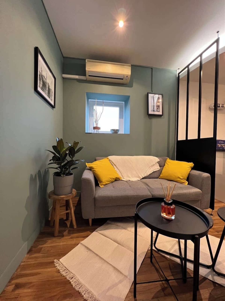 Séjour cosy avec canapé, table basse et verrière — mur vert et climatisation réversible au Câlin