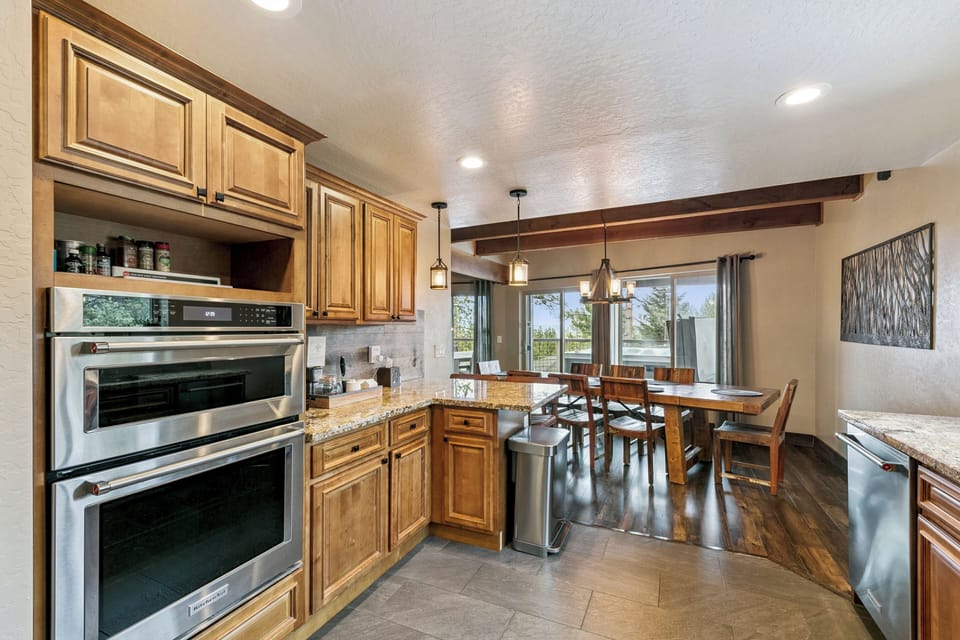 Your fully equipped kitchen features granite counters, stainless appliances, and rich wood cabinetry, flowing into a sunny dining area.