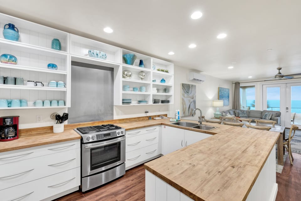 Your gourmet kitchen features modern appliances, butcher-block counters, and open shelving showcasing coastal-themed dishware.