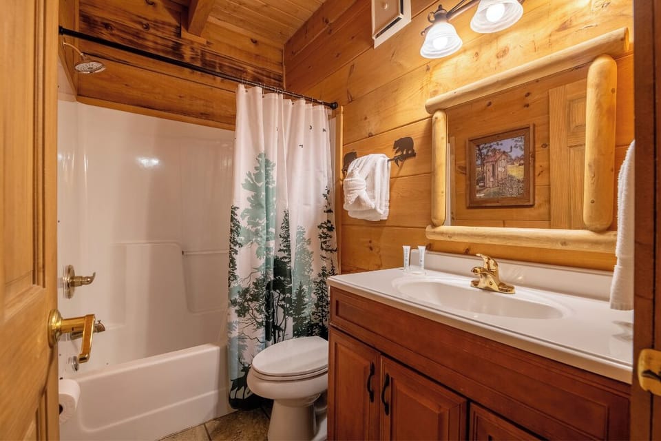 Your warm cabin bathroom features a tub-shower combo, fresh towels, and cozy wood paneling with rustic bear accents to make you feel right at home.
