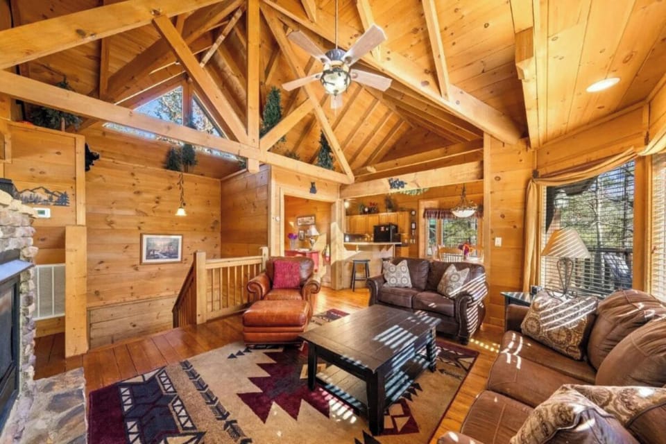 Relax in this stunning open-concept cabin living room with soaring wood-beamed ceilings and cozy leather seating around the warm fireplace.