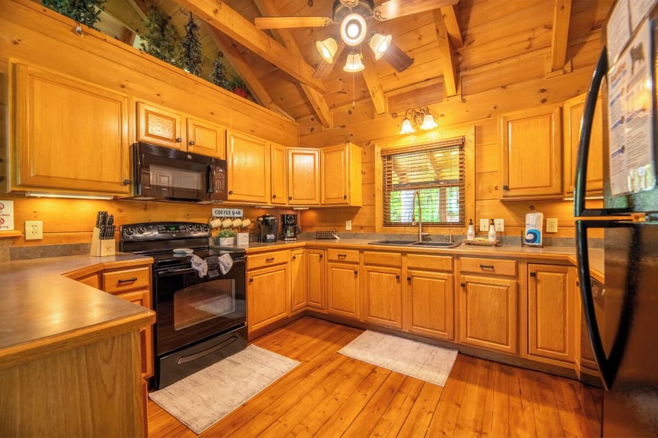 Picture yourself preparing meals in this charming cabin kitchen, where warm wood tones embrace modern appliances and a vaulted ceiling adds an airy, cozy feel to your mountain getaway.