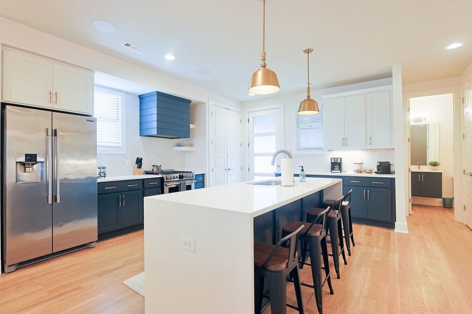 Wide view of the modern kitchen with stainless steel appliances, central island with bar seating, and open sightlines to the dining and living areas.