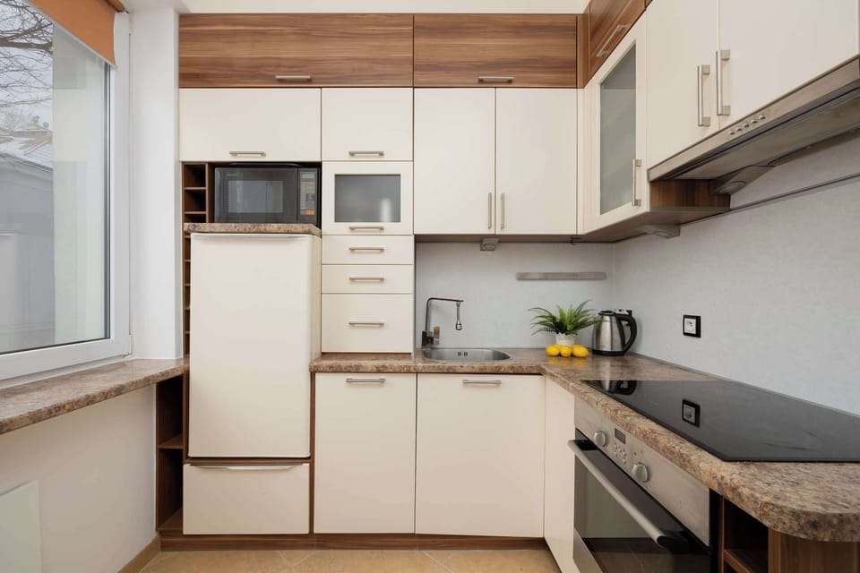 A kitchen interior with white cabinets and a wooden countertop. Appliances are built into the cabinetry for a clean look. The space feels organized and bright.