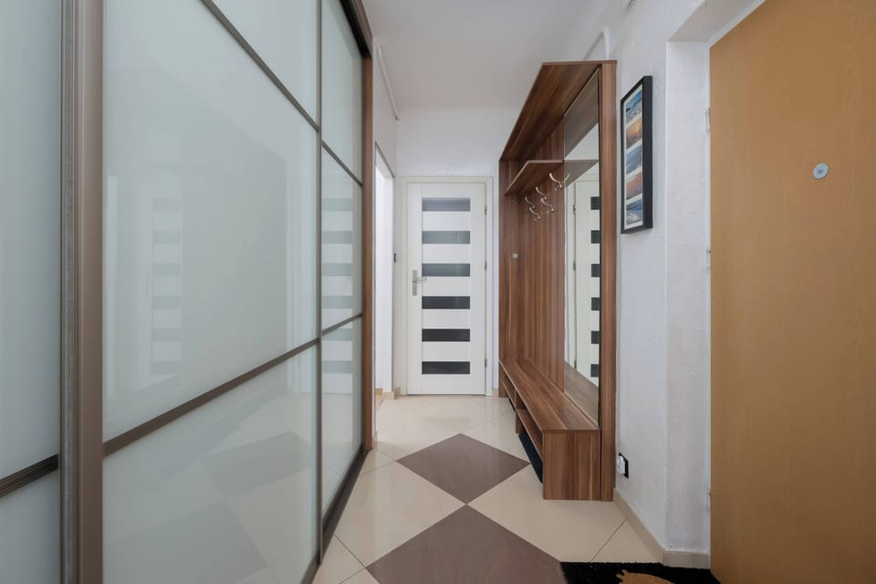 A hallway with sliding doors and light-colored walls. The wooden floor adds warmth to the interior. The passage feels clean and spacious.
