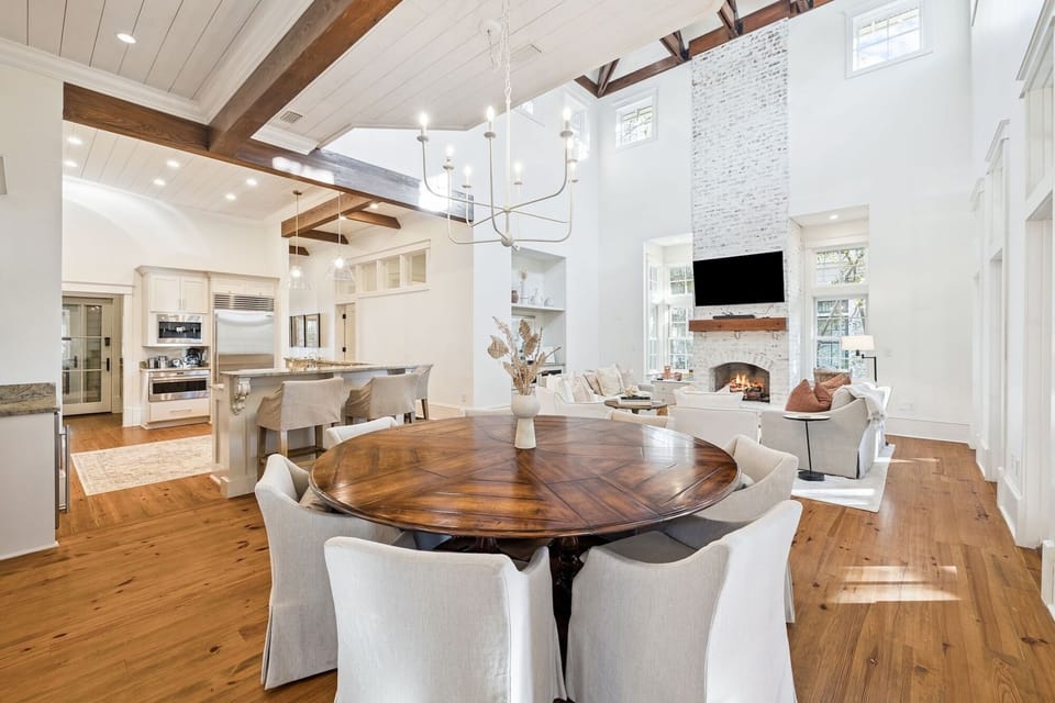 Step into your elegant open-concept haven where soaring ceilings and rich wood beams frame intimate dining moments by the cozy fireplace.