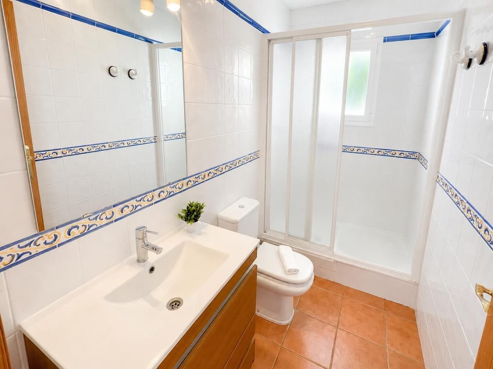 This contemporary Mediterranean villa bathroom features a sleek single vanity sink setup, classic terracotta floor tiles, and a private glass-enclosed shower stall designed for ultimate guest comfort.