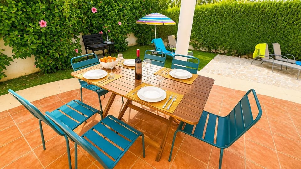 Outdoor dining patio with wooden table, teal chairs, and grill area.