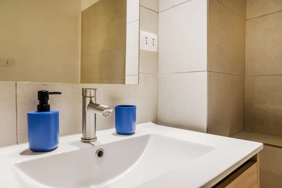 Bathroom vanity with a polished metal faucet, frameless mirror, and coordinated blue guest amenities.