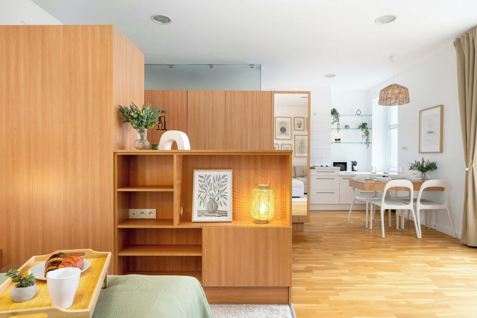 Functional studio layout combining double bed, sofa seating area, and built-in wooden shelving.