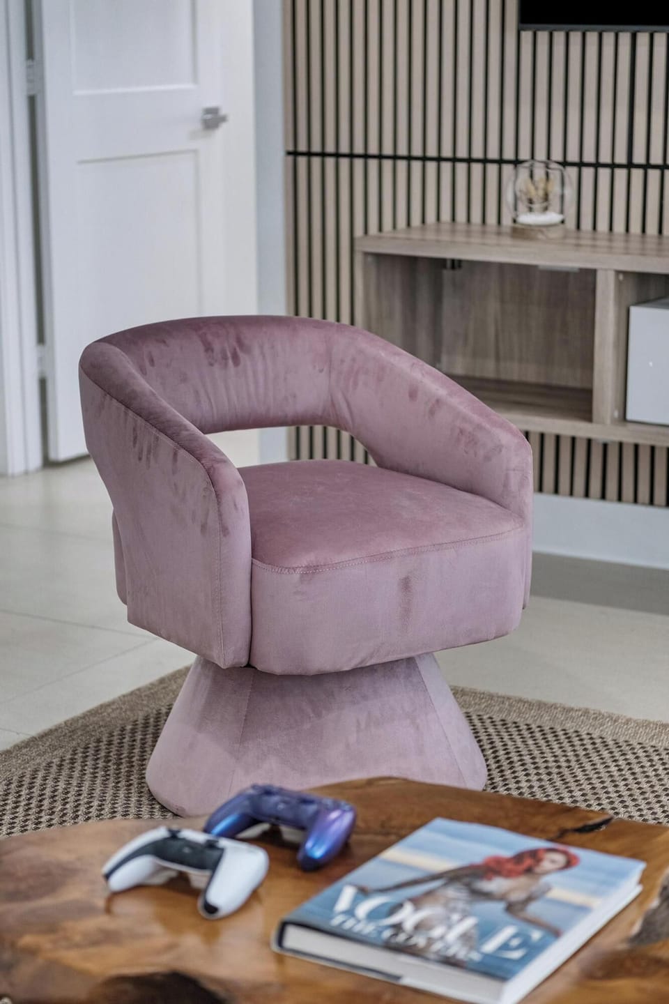 Modern mauve swivel chair in a stylish living area with gaming controllers and a magazine on a wooden table