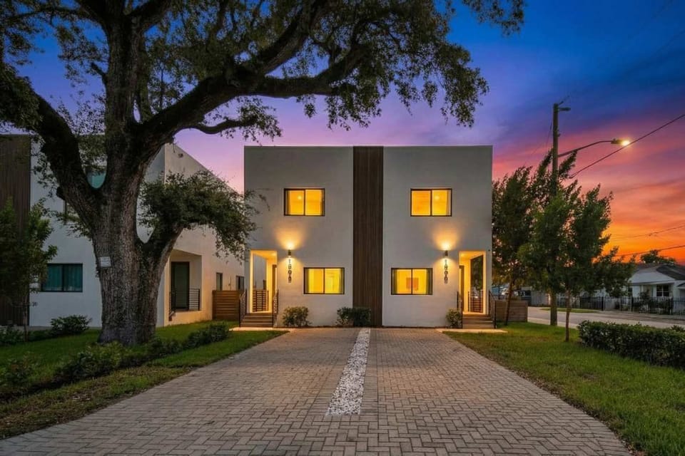 Warm exterior shot at dusk — glowing windows & lush landscaping welcome you in.
