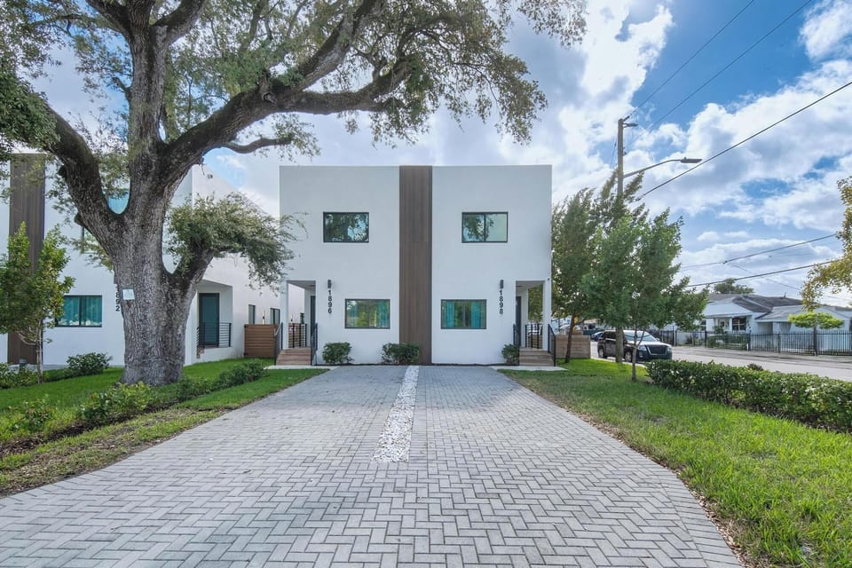 Modern white duplex with a spacious paved driveway and mature trees