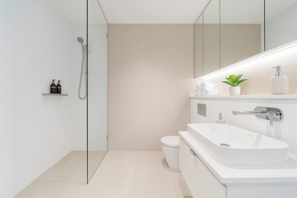 Bathroom with a walk in shower featuring a hand held shower on a slide rail and a wall shelf. Floating white vanity with vessel basin, concealed cistern toilet, and LED lit mirror cabinet above.