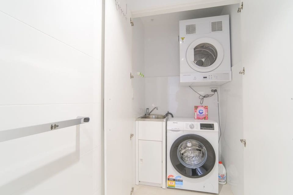 Laundry closet with a wall mounted dryer above a front loading washing machine, alongside a stainless laundry tub with a mixer tap.