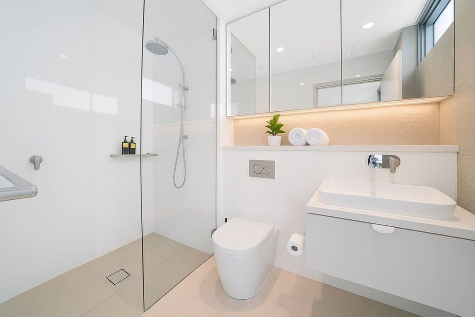 Second bathroom with a walk in shower featuring a rainfall shower head and hand held shower on a slide rail. Floating vanity with vessel basin and wall mounted tap, concealed cistern toilet, and LED lit mirror cabinet.