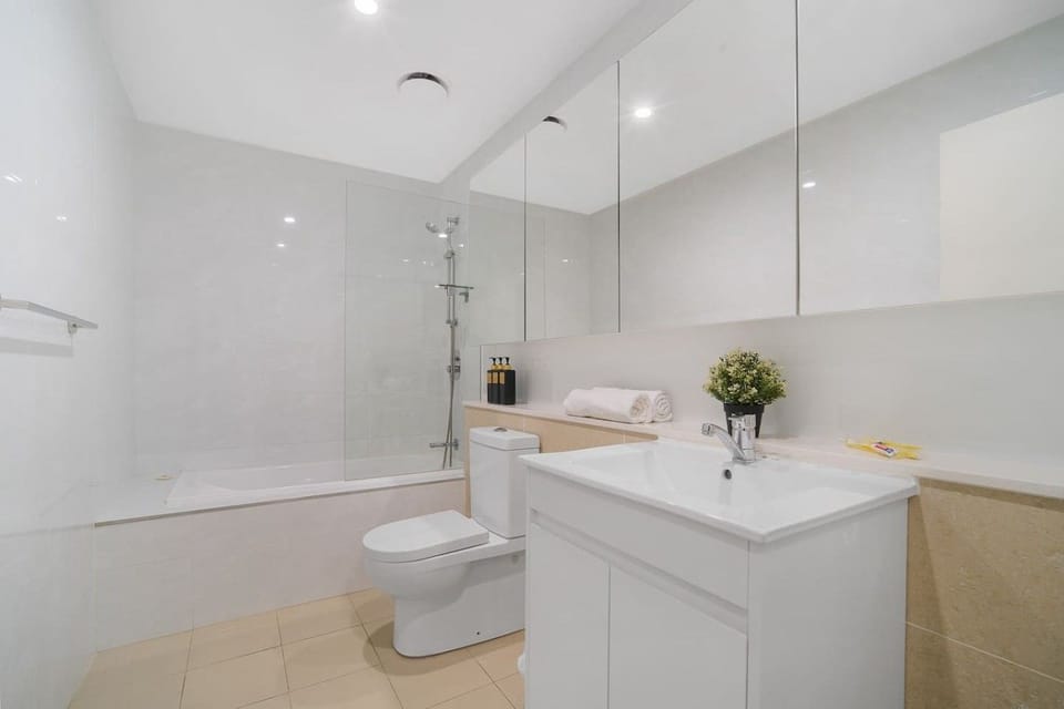 Bathroom with a bath, a shower over it behind a glass screen, a toilet and a vanity with a mirrored cabinet above. Towels and toiletries on the shelf.