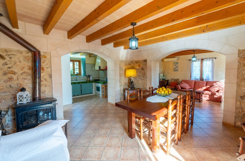 Open-plan space with dining area, cozy living room, integrated kitchen and wood-burning stove at Villa Sa Mata in Mallorca.