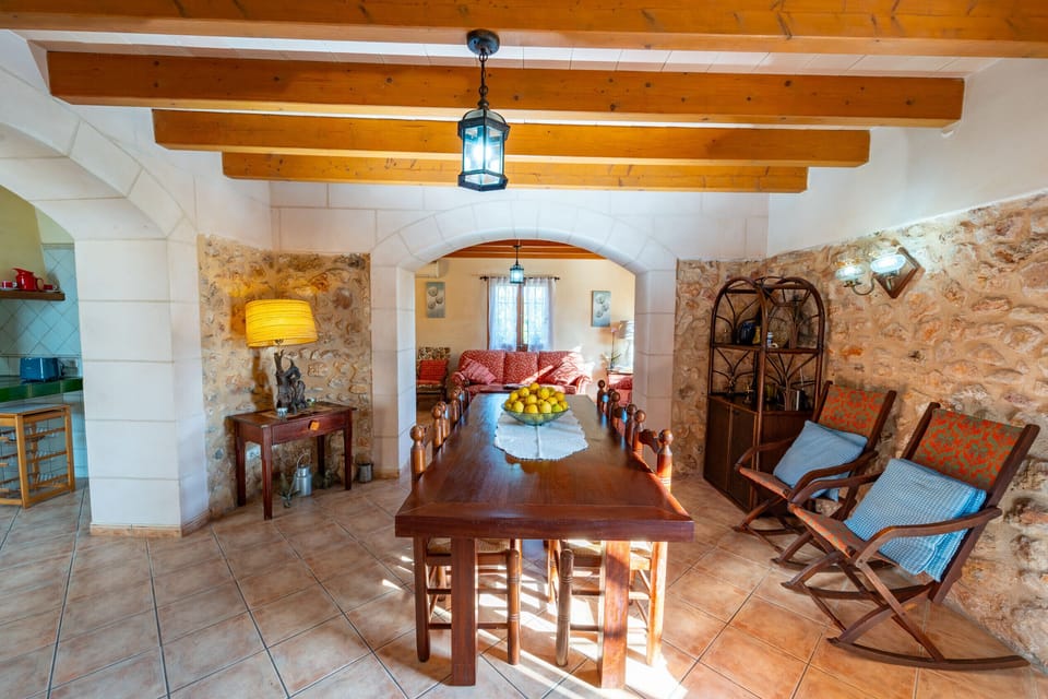 Spacious rustic dining room with wooden table, exposed beams and stone arch leading to the living room at Villa Sa Mata in Mallorca.