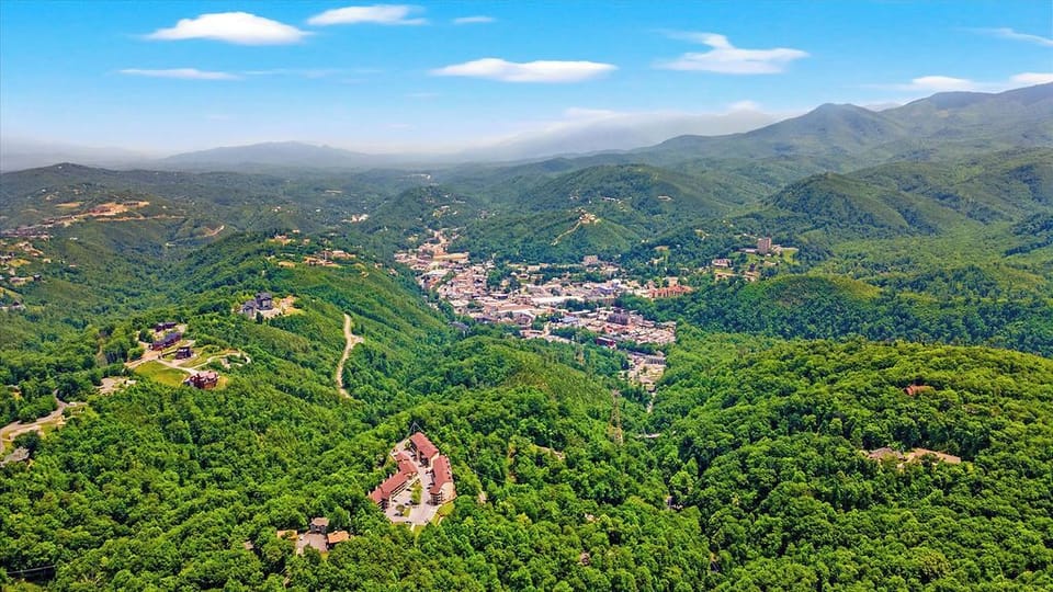 Aerial view showcasing the property nestled among rolling green mountains and a nearby charming town, surrounded by pristine natural landscapes.