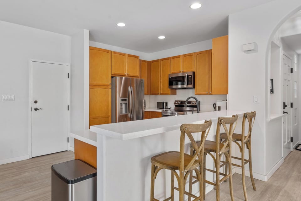 Your modern kitchen features warm wood cabinets, sleek appliances, and a breakfast bar perfect for morning coffee or casual meals.